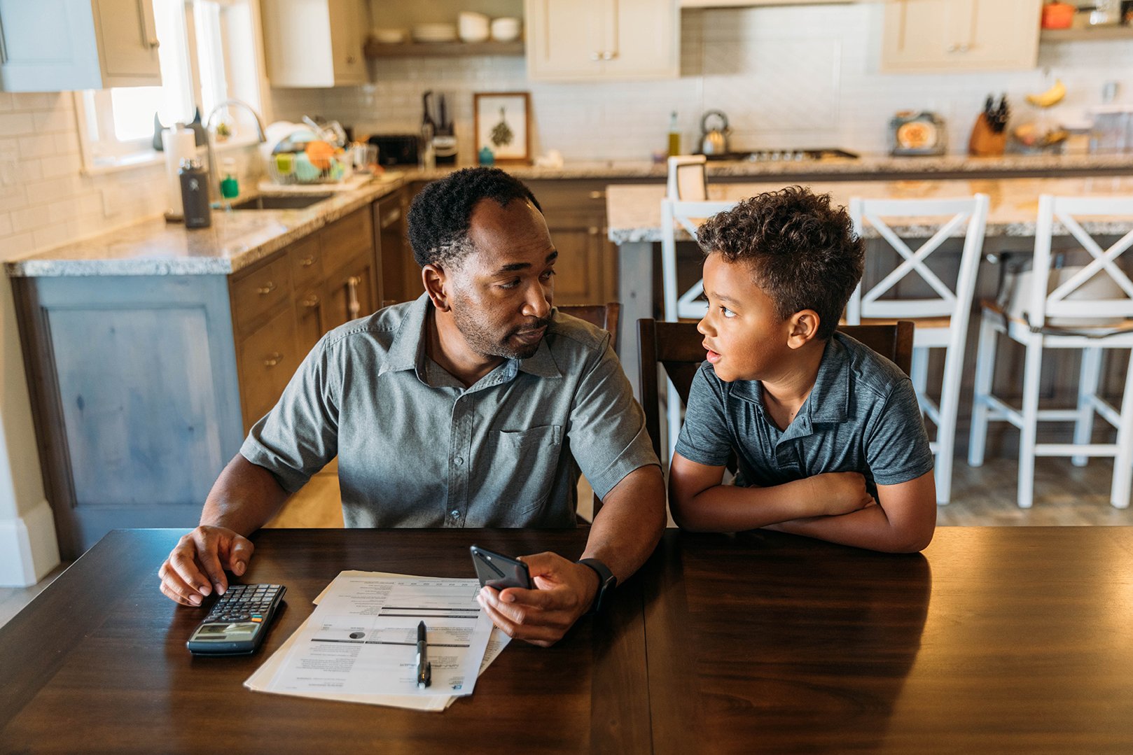Dad sitting at kitchen table talking to his son.